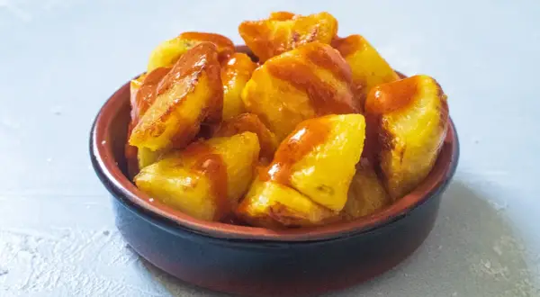Knusprige Kartoffelstücke, überzogen mit einer würzigen Sauce, serviert als köstliche Patatas Bravas in einer kleinen Schale.