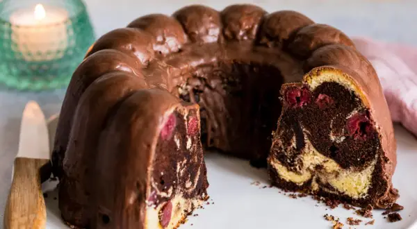 Ein saftiger Marmorkuchen mit Kirschen, überzogen mit Schokoladenglasur, auf einem weißen Teller.