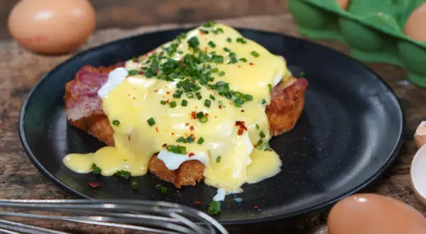 Ein köstliches Egg Benedict mit pochiertem Ei, Speck und Sauce Hollandaise, garniert mit Schnittlauch und Chiliflocken.