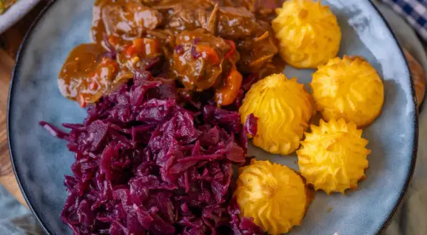 Herzoginkartoffeln selber machen ist einfach! Hier sind sie mit deftigem Gulasch und Rotkohl auf einem Teller angerichtet.