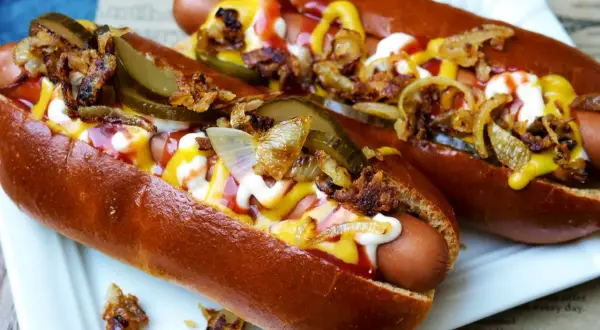 Zwei appetitliche Hot Dogs mit Senf, Ketchup, Mayonnaise, Gurken und Röstzwiebeln.