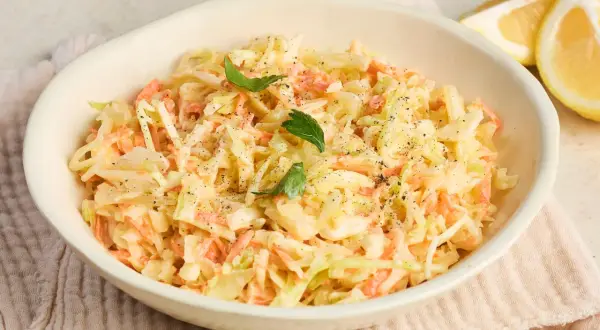 Cremiger Coleslaw Salat mit Karotten und Kohl, garniert mit Petersilie und Pfeffer. Dazu Zitronenspalten.