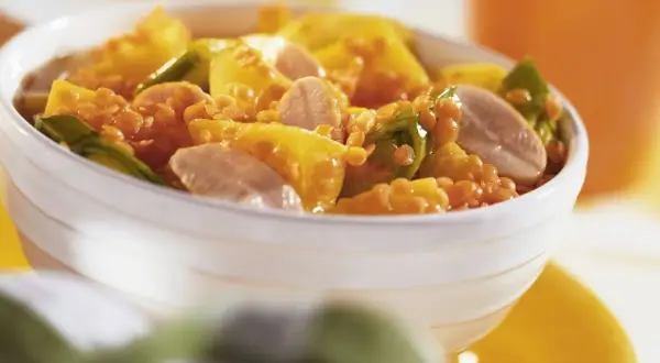Schüssel mit einem leckeren roten Linsen Rezept, garniert mit gelben Paprikastücken und Fleischstreifen.