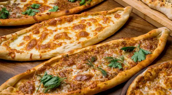 Mehrere Pide-Gerichte, darunter eines mit Käse und eines mit Hackfleisch, sind auf einem Holztisch angerichtet. Ein köstliches Pide Rezept!