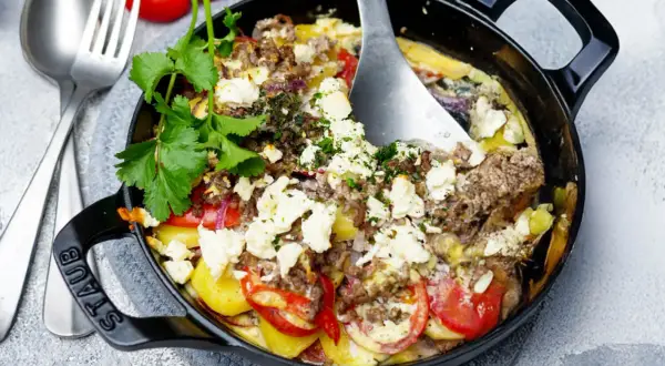 Herzhaft gebackener Feta mit Hackfleisch, Kartoffeln und Tomaten in einer schwarzen Gusseisenpfanne, garniert mit frischer Petersilie.