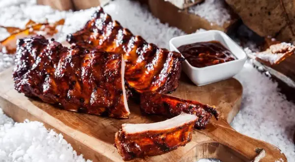 Saftige spareribs im backofen, glasiert und mit BBQ-Sauce, auf einem Holzbrett im Schnee.