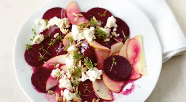 Rote Bete Salat mit Apfel, zerbröckeltem Käse und Sonnenblumenkernen auf einem weißen Teller.