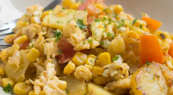 Herzhaftes Gericht mit Kartoffelscheiben, Rührei, Mais und Tomaten. Ein leckeres Beispiel für Kartoffel Gerichte.