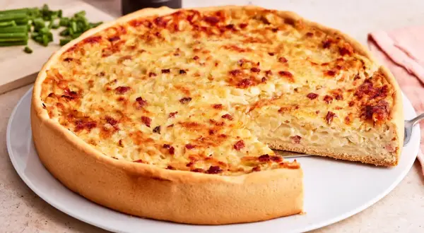 Ein goldbrauner Zwiebelkuchen mit Speck, ein Stück herausgeschnitten. Perfekt für ein Zwiebelkuchen Rezept.