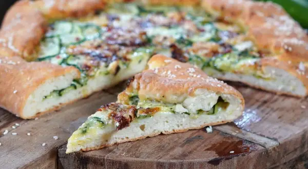 Eine köstliche Zucchini-Pizza mit goldbraunem Teig und saftiger Füllung, auf einem rustikalen Holzbrett serviert.