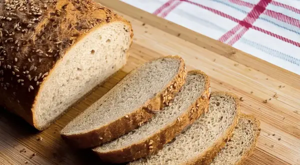 Ein frisch gebackenes Brot, perfekt für ein keto brot rezept, liegt auf einem Holzbrett. Mehrere Scheiben sind bereits abgeschnitten.