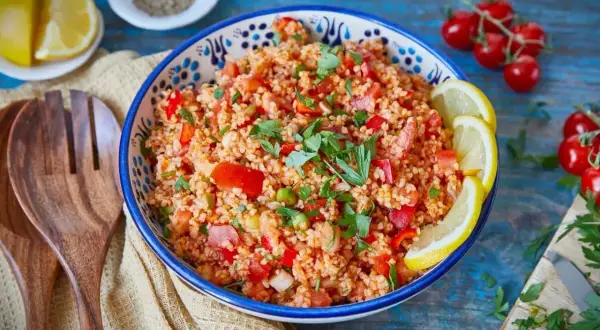 Frischer Bulgur Salat mit Tomaten, Paprika und Kräutern, garniert mit Zitronenspalten. Ein leichter Genuss!