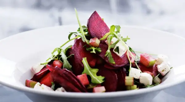 Ein köstlicher rote beete salat mit Rucola, Feta und Apfelstücken in einer weißen Schüssel.
