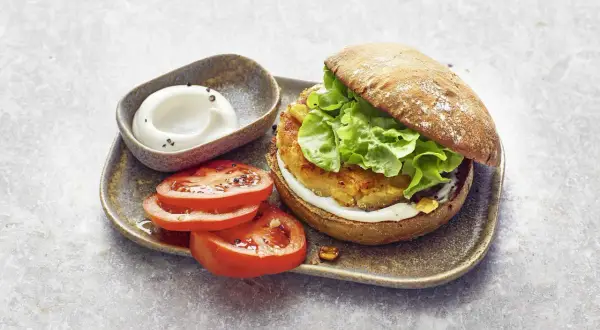 Ein saftiger vegetarischer Burger mit knackigem Salat, dazu frische Tomatenscheiben und eine cremige Sauce. Ein Genuss für alle Sinne!