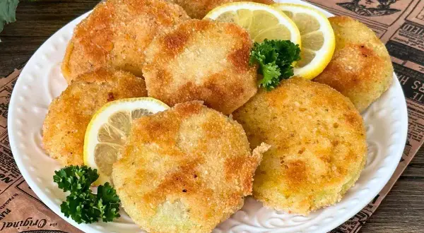 Knusprige Kohlrabi-Schnitzel auf einem Teller mit Zitronenscheiben und Petersilie garniert. Ein köstliches vegetarisches Gericht.