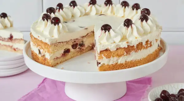 Saftiger Kuchen mit Sahne und Kirschen, perfekt zum Amarenakirschen selber machen. Ein Stück fehlt, daneben eine Schale mit Kirschen.