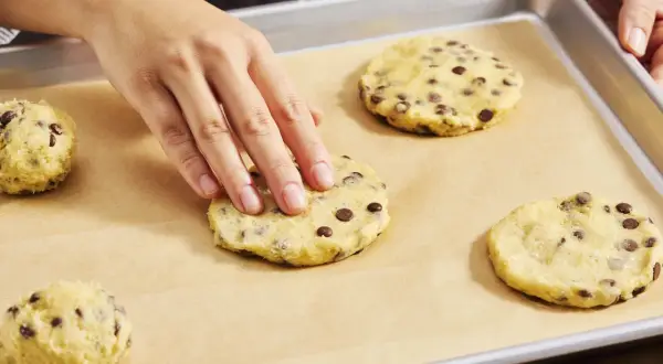 Hände formen Teig für Chocolate Chip Cookies auf einem Backblech. Der Teig ist voller Schokoladenstückchen, bereit für den cookie crumble.