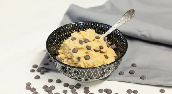 Schüssel mit essbarem Keksteig und Schokostückchen, daneben verstreute Schokotropfen. Ein Löffel steckt im Teig.