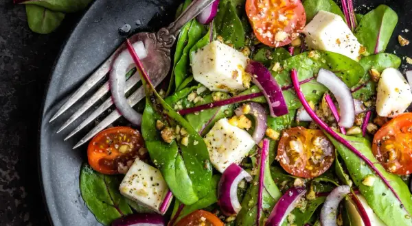 Frischer mangold salat mit Kirschtomaten, roter Zwiebel und Feta-Käse, garniert mit Nüssen und einem Dressing.