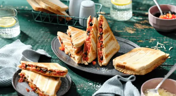 Leckere Sandwichmaker Rezepte: Getoastete Sandwiches mit Tomaten und Oliven, serviert mit Zitrone-Wasser.