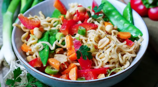 Bunter mie nudel salat mit Erdnüssen, Paprika, Zuckerschoten und Karotten, garniert mit Petersilie.