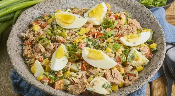 Herzhafter Thunfischsalat mit Mais, Tomaten, Ei und Frühlingszwiebeln, garniert mit hartgekochten Eierspalten.