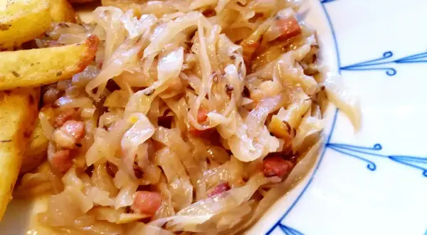 Herzhaftes bayrisch Kraut mit Speckwürfeln, serviert mit knusprigen Kartoffelspalten und einer Wurst. Ein Klassiker!