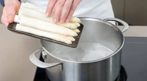 Frischer weißer Spargel wird in kochendes Wasser gegeben. So beginnt das Spargel kochen mit oder ohne Deckel.