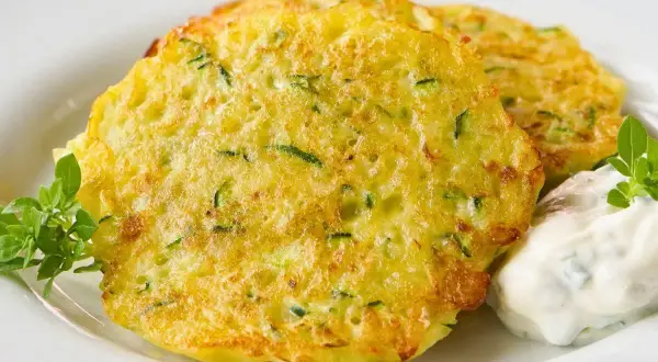 Goldbraune Zucchini-Puffer mit Kräuterquark und frischem Grün.