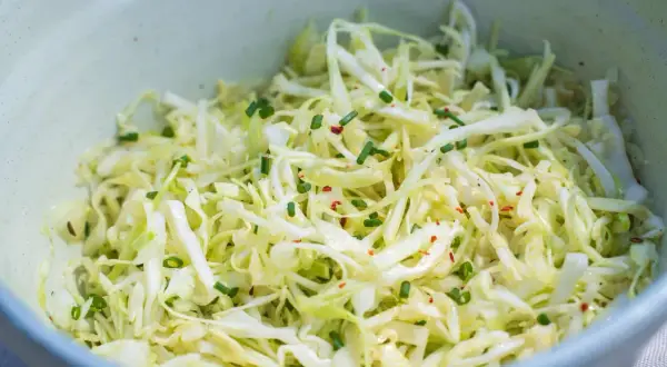 Frischer Spitzkohl Salat, fein geschnitten und mit Schnittlauch und Chiliflocken garniert, wartet in einer Schüssel.
