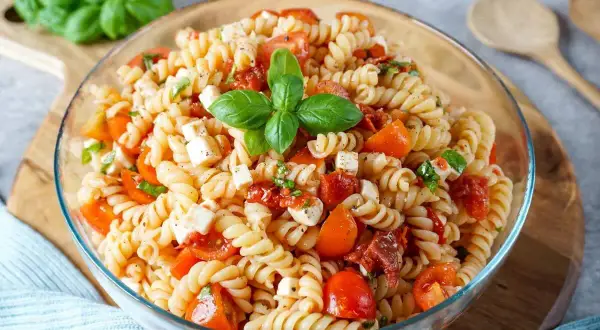 Ein köstlicher mediterraner Nudelsalat mit Fusilli, Kirschtomaten, Mozzarella und frischem Basilikum, garniert mit einem Basilikumblatt.
