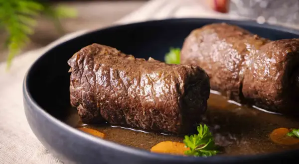 Zwei saftige Rouladen im Schnellkochtopf, serviert mit Karottenstücken und Petersilie in einer dunklen Sauce.
