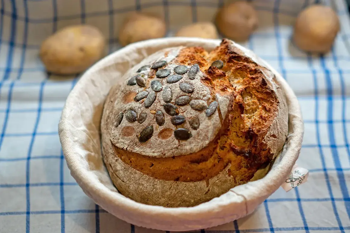 Ein frisch gebackenes Kartoffelbrot mit Kürbiskernen, bereit für das Kartoffelbrot Rezept. Kartoffeln liegen unscharf im Hintergrund.