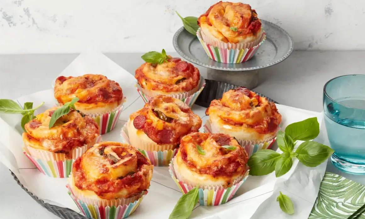 Leckere Pizza Muffins mit Salami und Käse, garniert mit frischem Basilikum.