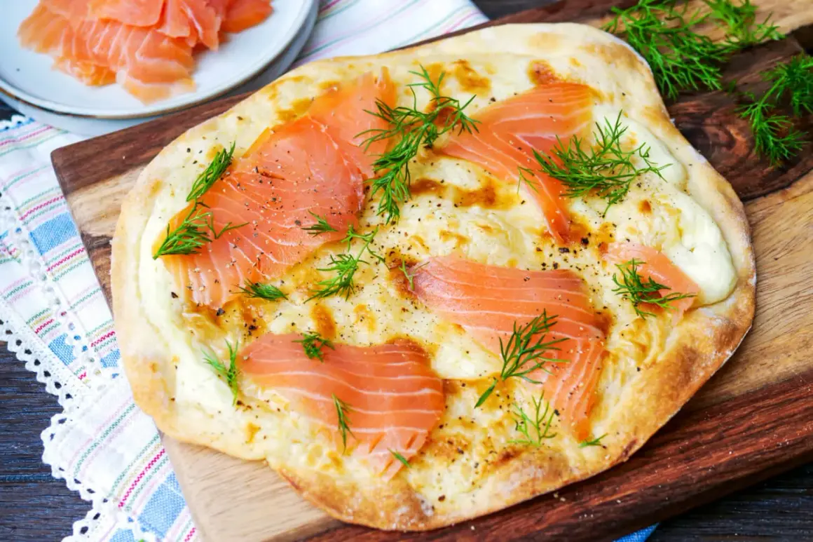 Flammkuchen mit Lachs, belegt mit zarten Lachsscheiben, geschmolzenem Käse und frischem Dill, garniert mit Pfeffer.