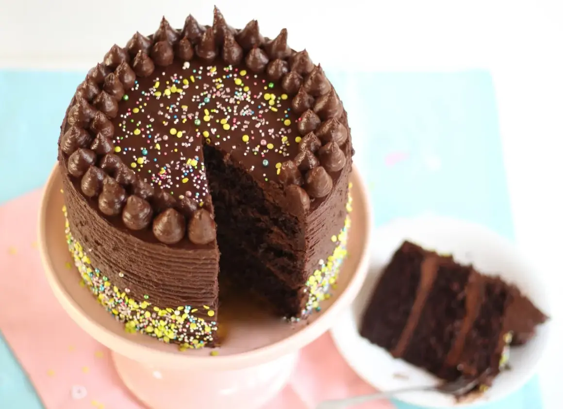 Eine köstliche Schokocreme Torte mit bunten Streuseln und Schokostückchen. Ein Stück ist bereits angeschnitten.