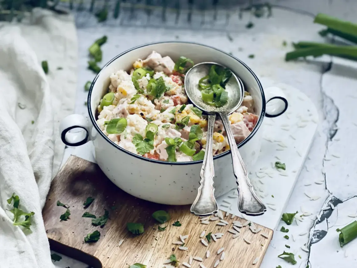 Ein cremiger Reis-Salat mit Hähnchen, Mais und Tomaten, garniert mit Frühlingszwiebeln und Petersilie. Perfekt für ein leichtes Mittagessen.