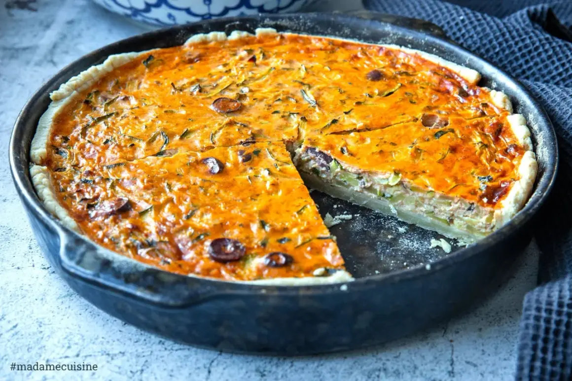 Eine köstliche Zucchini-Quiche mit Oliven in einer Gusseisenpfanne, eine Scheibe herausgeschnitten.