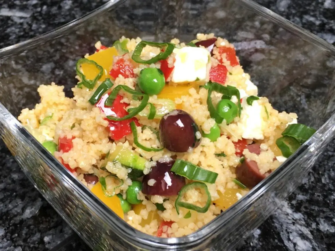 Frischer Couscous Salat mediterran mit Oliven, Paprika, Erbsen und Feta in einer Glasschüssel.
