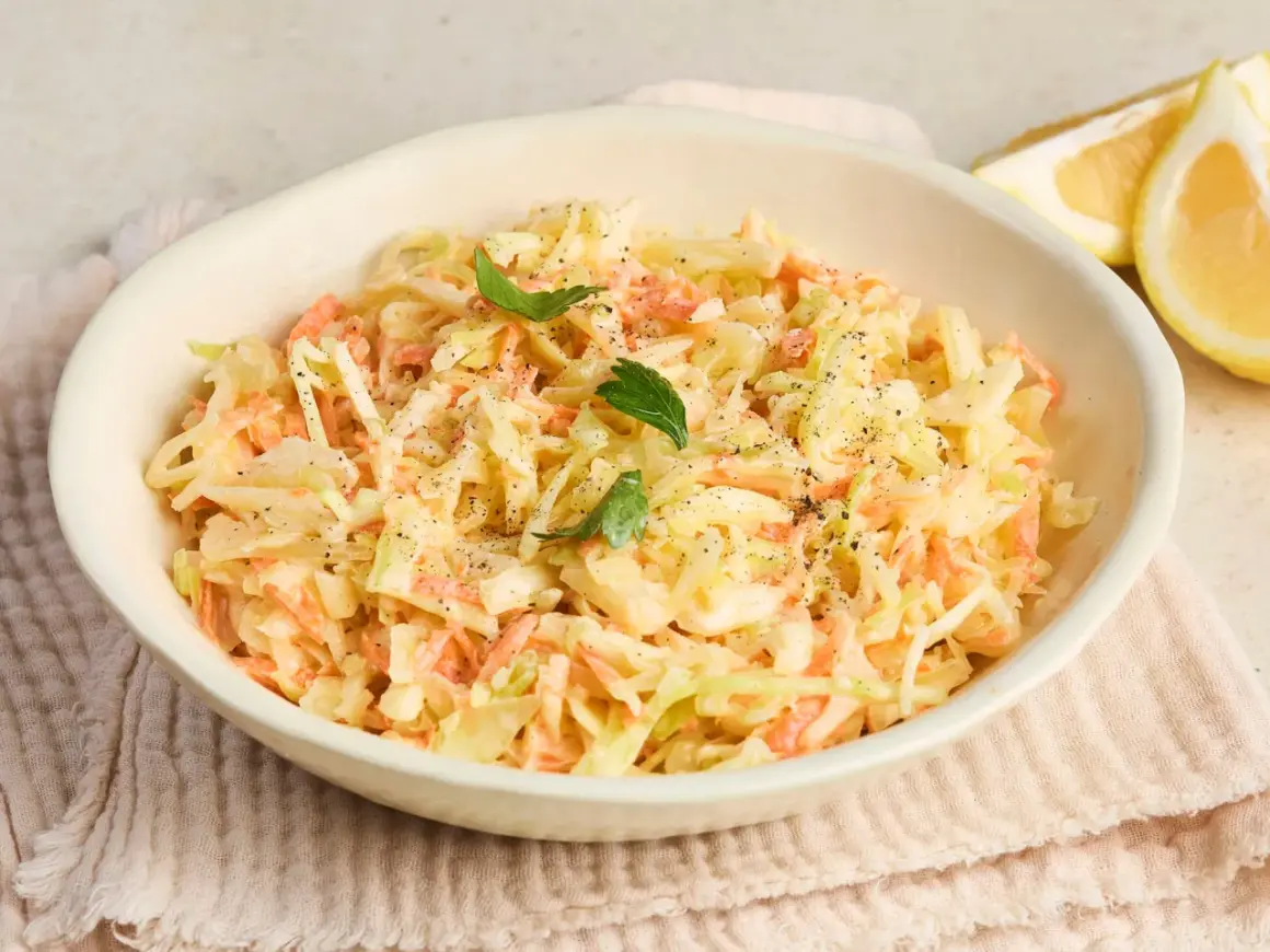 Cremiger Coleslaw Salat mit Karotten und Kohl, garniert mit Petersilie und Pfeffer. Dazu Zitronenspalten.