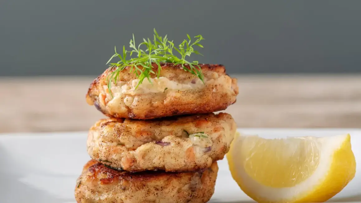 Gestapelte Fischbuletten, garniert mit Dill, neben einer Zitronenspalte. Ein leckeres Buletten Rezept.