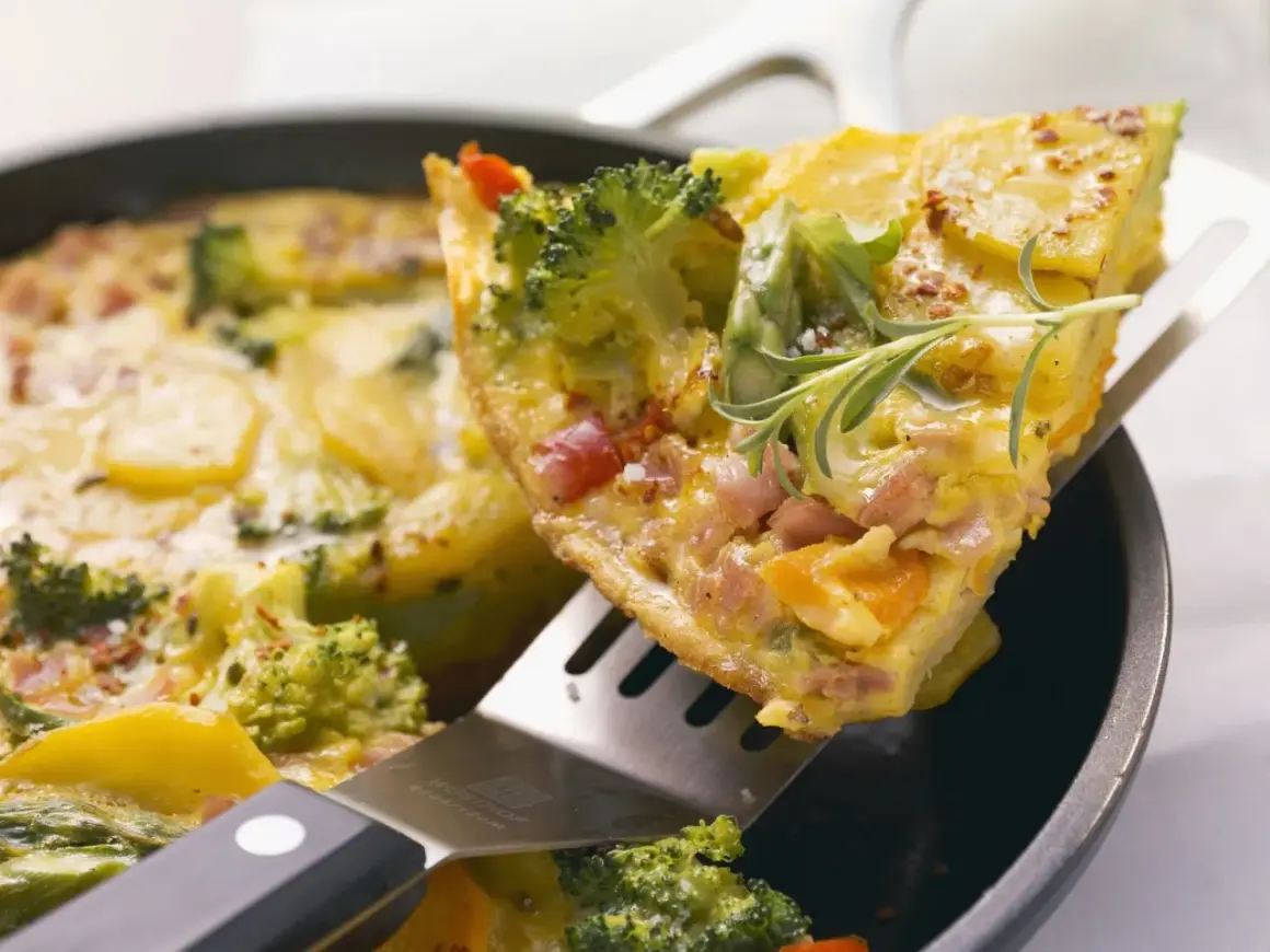 Ein Stück herzhaftes Omelett mit Brokkoli, Kartoffeln und Schinken wird aus einer Pfanne gehoben. Ein tolles Omelett Rezept für jeden Tag.