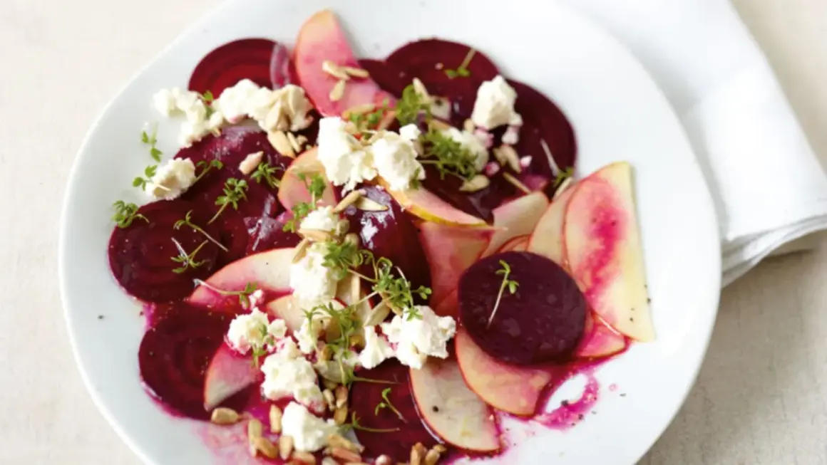 Rote Bete Salat mit Apfel, zerbröckeltem Käse und Sonnenblumenkernen auf einem weißen Teller.