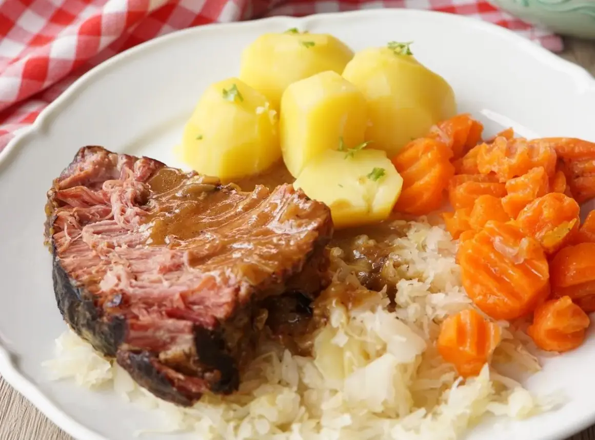 Saftiger Kassler im Ofen mit Salzkartoffeln, Möhren und Sauerkraut. Ein deftiges Gericht, das auf der Zunge zergeht.