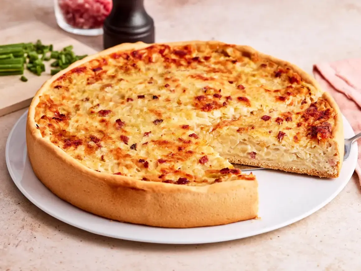 Ein goldbrauner Zwiebelkuchen mit Speck, ein Stück herausgeschnitten. Perfekt für ein Zwiebelkuchen Rezept.