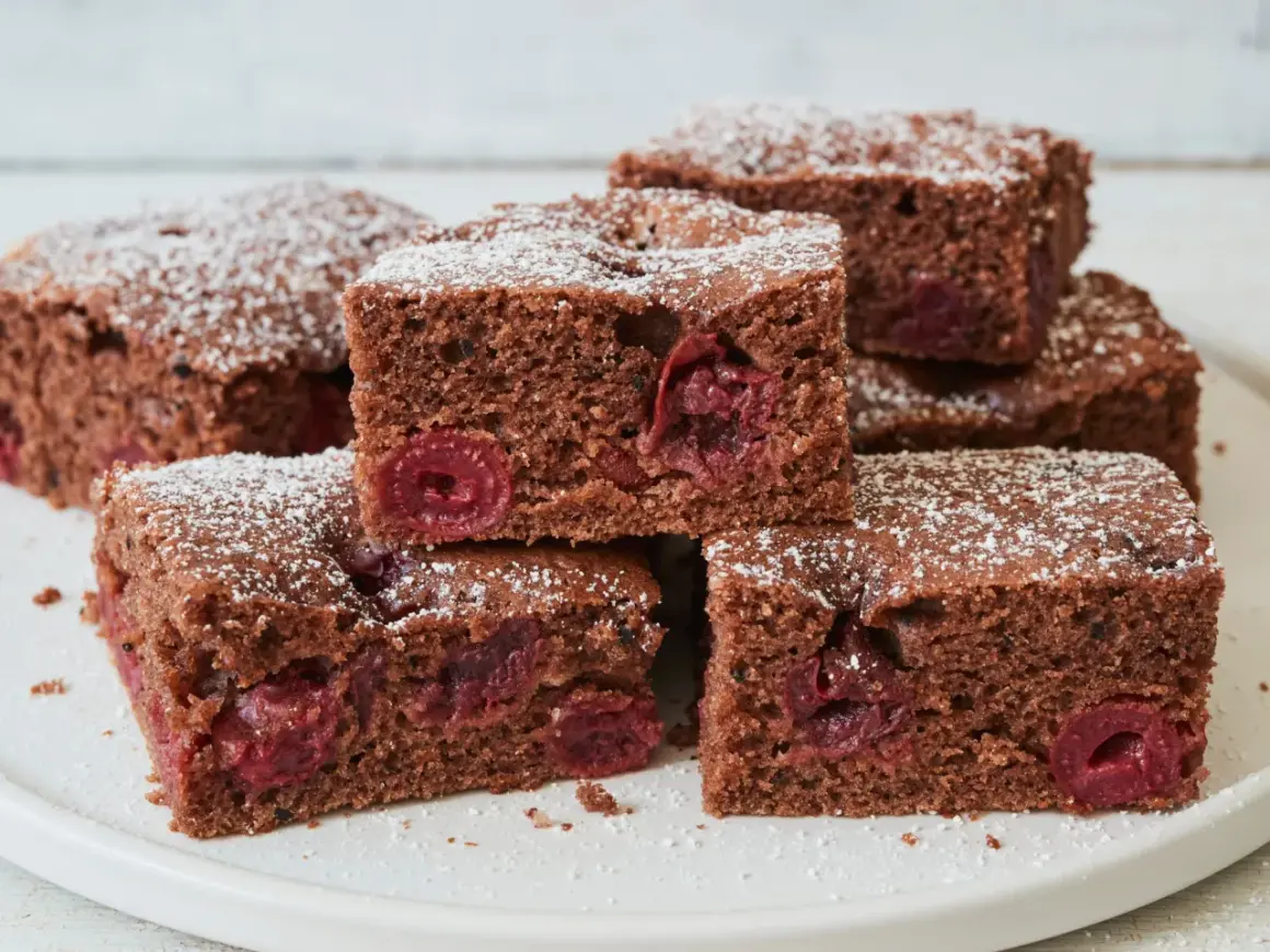 Saftiger Schokokuchen vom Blech mit Kirschen, bestäubt mit Puderzucker. Ein Genuss für jeden Schokoladenliebhaber.