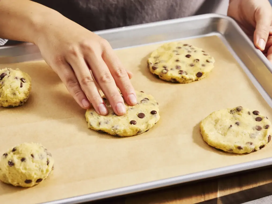 Hände formen Teig für Chocolate Chip Cookies auf einem Backblech. Der Teig ist voller Schokoladenstückchen, bereit für den cookie crumble.