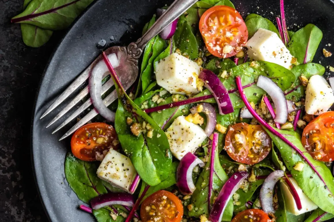Frischer mangold salat mit Kirschtomaten, roter Zwiebel und Feta-Käse, garniert mit Nüssen und einem Dressing.