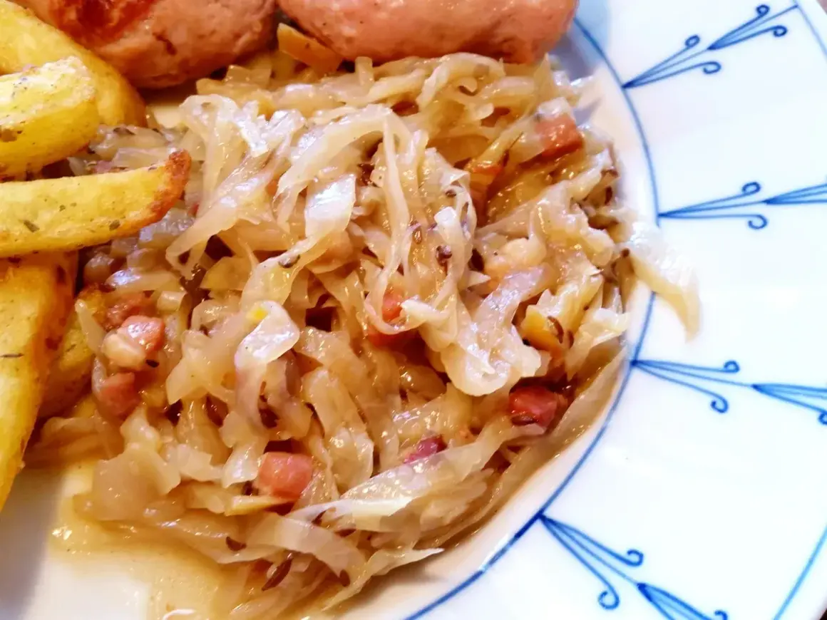 Herzhaftes bayrisch Kraut mit Speckwürfeln, serviert mit knusprigen Kartoffelspalten und einer Wurst. Ein Klassiker!