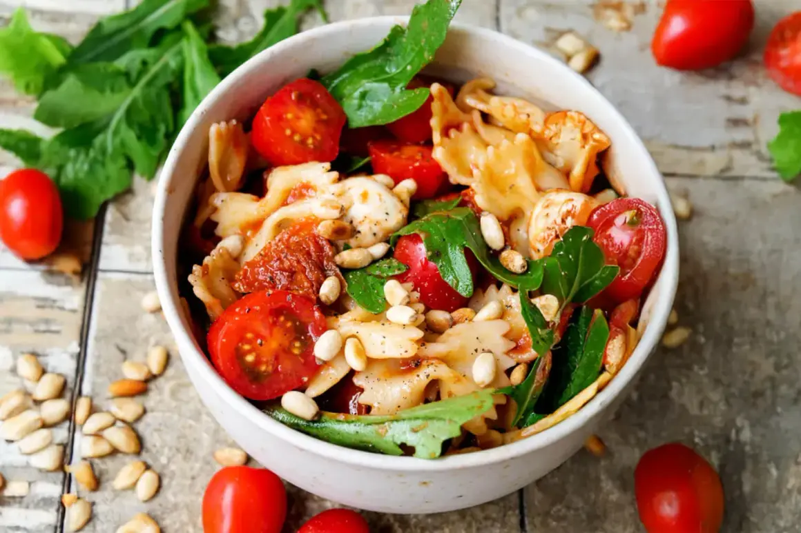 Schüssel mit Nudelsalat, Farfalle, Kirschtomaten, Mozzarella, Pinienkernen und Rucola. Ein köstlicher nudelsalat mit getrockneten tomaten.